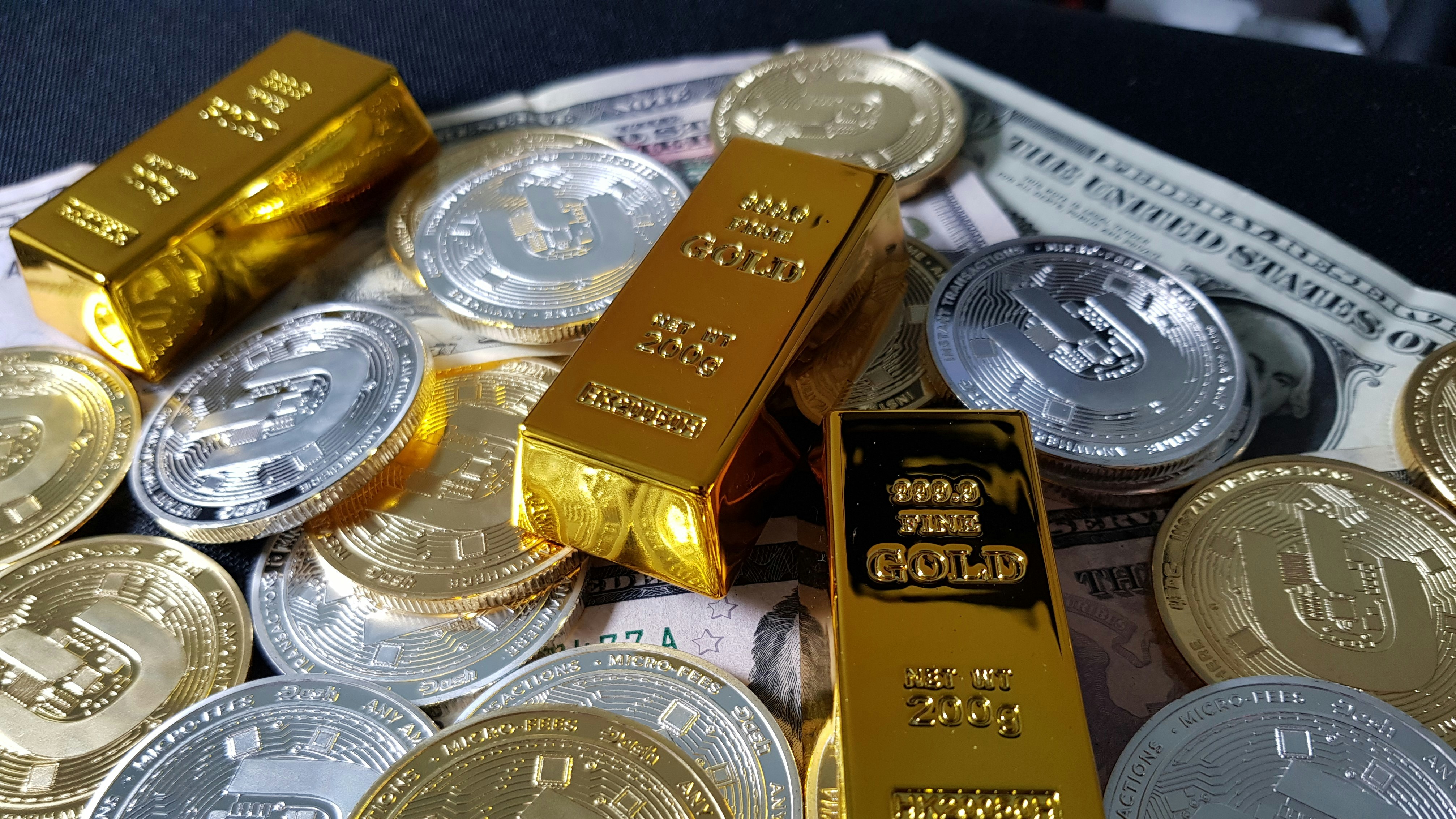 Several gold bars are placed on top of a pile of bitcoin coins and US dollar bills, indicating a scene of wealth and finance.